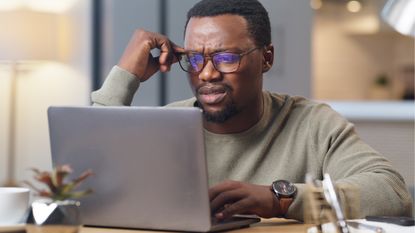 A middle-aged man looks stressed as he looks at his laptop at home.