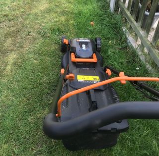 Worx cordless lawn mower cutting next to a fence