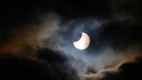 partial solar eclipse appearing from behind some broken cloud.