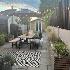 garden space with outdoor rug, dining table and parasol with bistro lights