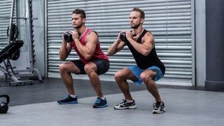 Two men squatting with a kettlebell using goblet hold during workout