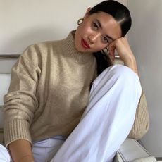 woman in a spring outfit with gold earrings, beige turtleneck and white jeans