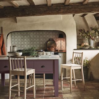 farmhouse style rustic kitchen with beams, tiled splashback, aubergine painted kitchen island, pale wood stools, terracotta style tiles