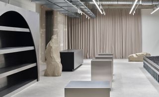 Alternative interior view of a store in Stuttgart designed by Vaust studio featuring light coloured walls and floors, an arched display area, steel stands, a display case filled with black granite and large faux stones made from Styrofoam
