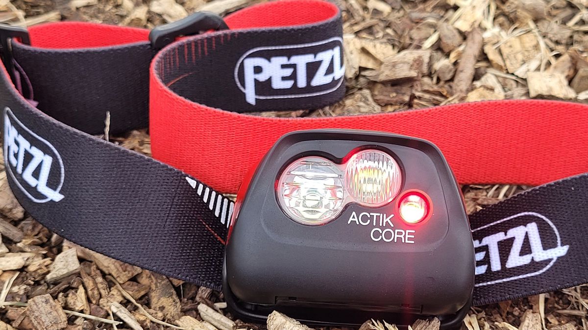 Petzl Actik Core 450 headlamp resting on wood chippings with the red light on.