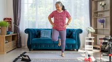 Woman performing step workout in living room, looking at tablet on floor