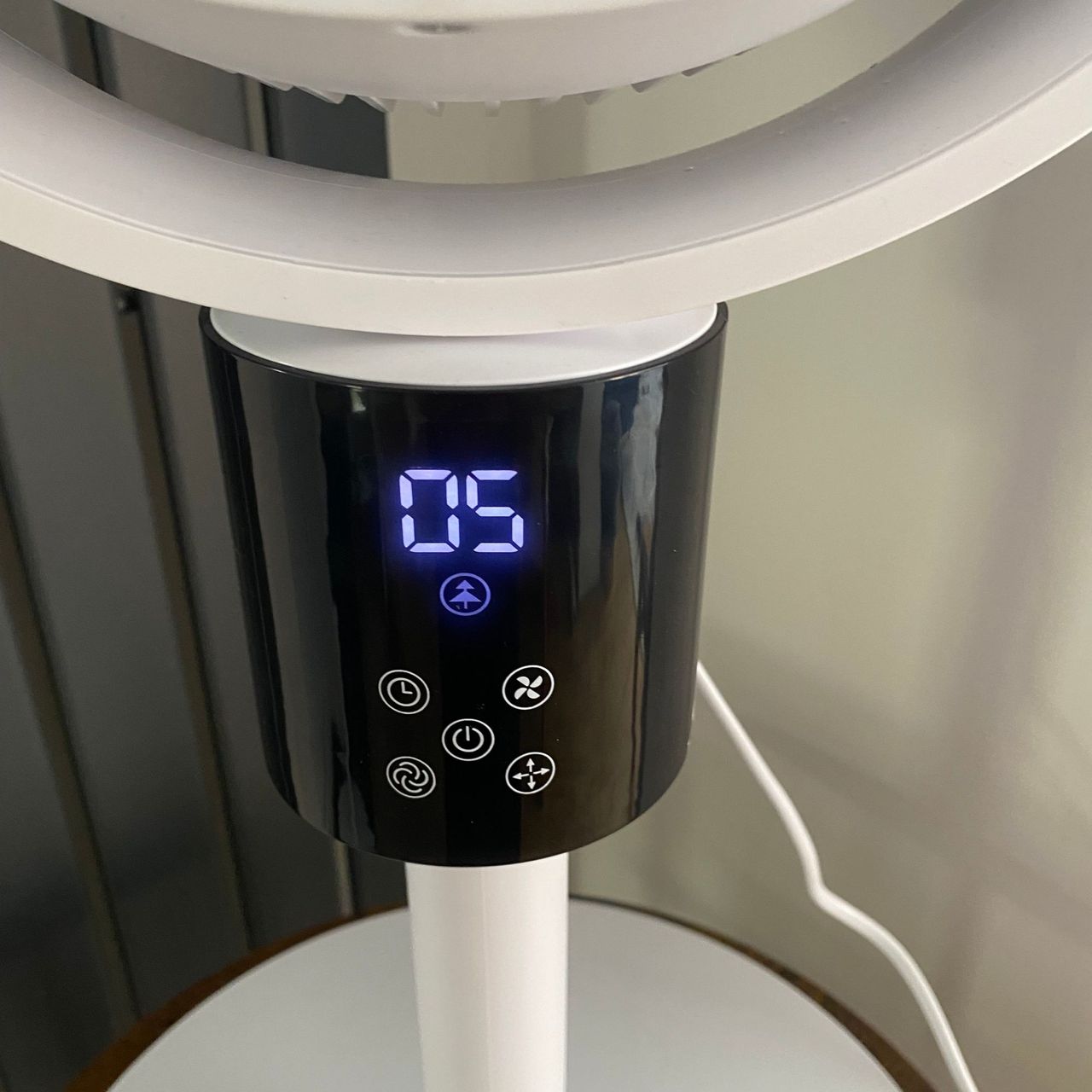 Close up of the display panels of the Silentnight Airmax Pro360 Pedestal Fan in Natural Wind mode, next to a vertical radiator