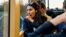 Woman yawning with headphones in on train around other people, representing hormone imbalance symptoms in women