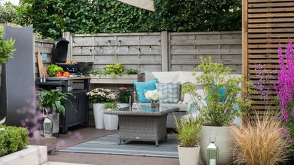 Gardens with ornamental grasses in pots around a BBQ area with festoon lighting and outdoor sofa