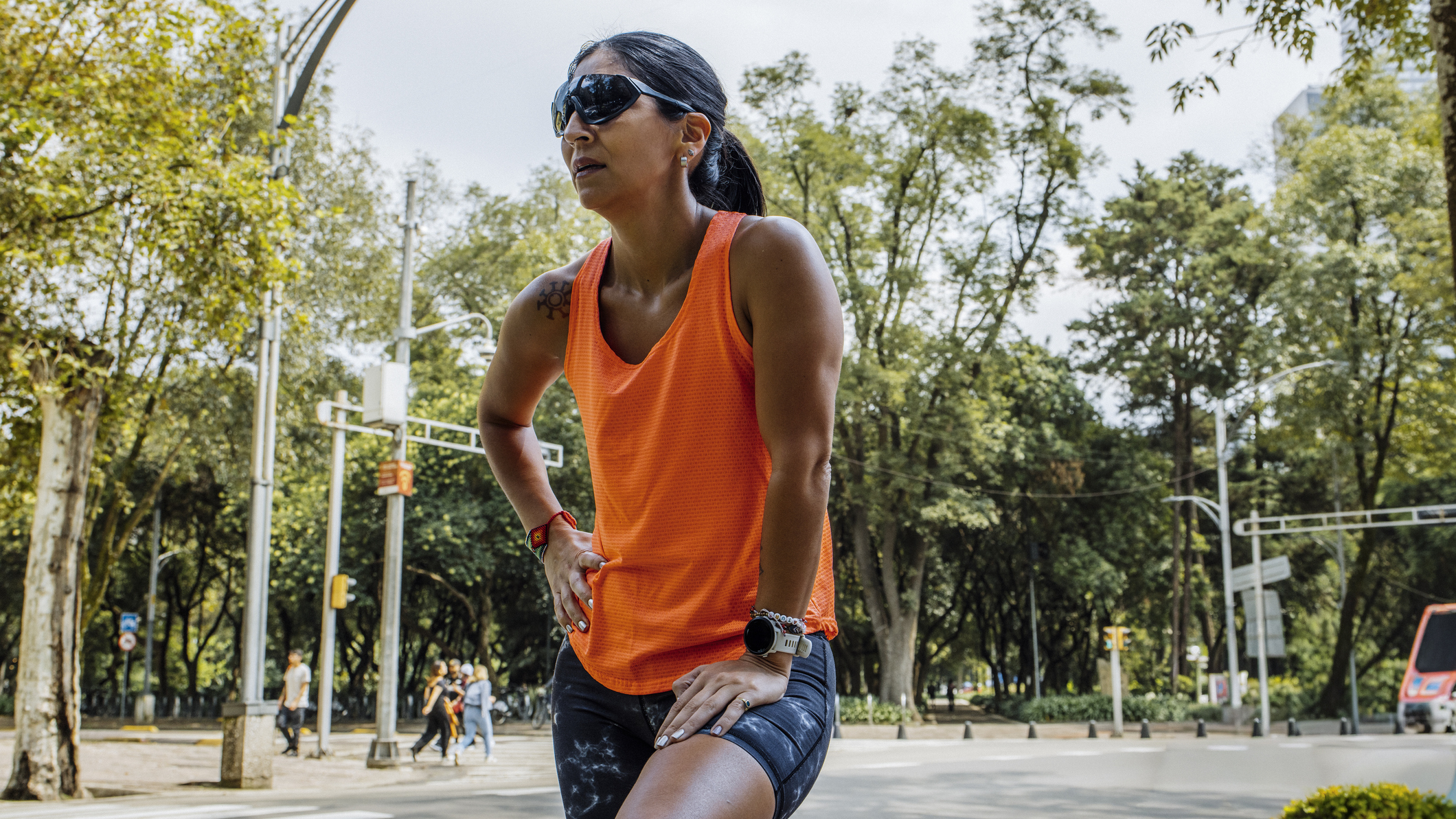 Woman in running clothes and sunglasses stands with one hand on her thigh