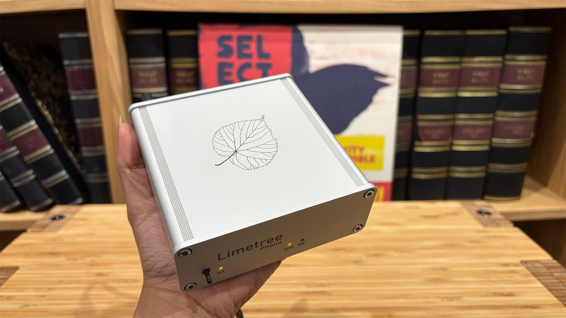 Lindemann Limetree Phono II phono stage held in hand in front of bookcase