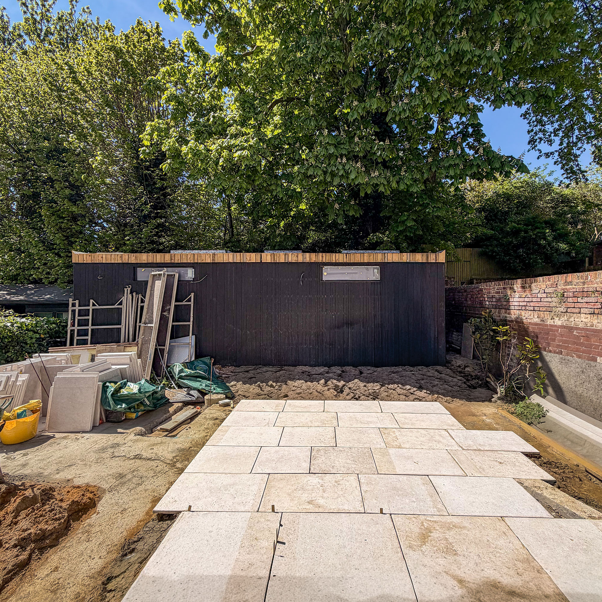 Summerhouse being built in front of trees in garden, with patio being paved in front