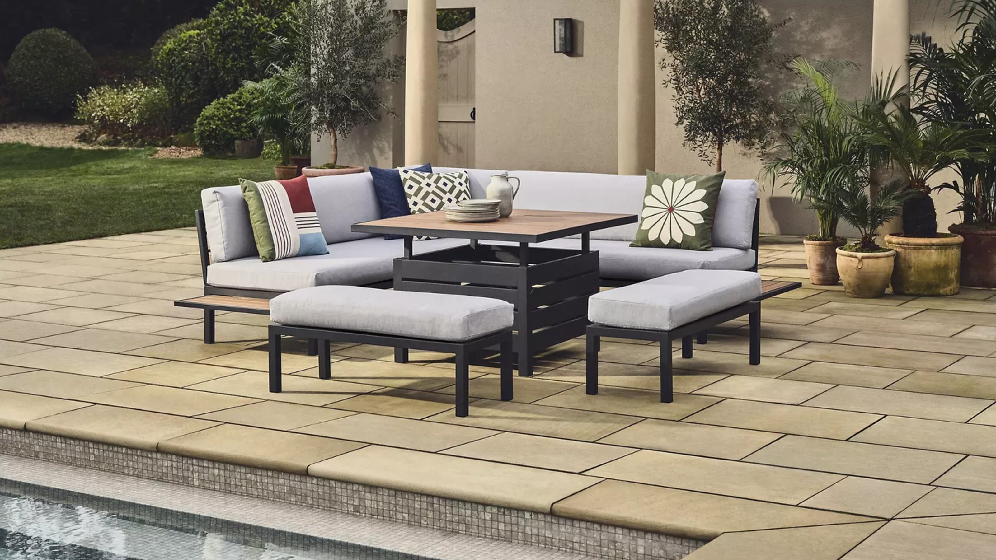 John Lewis Platform 8-Seater Corner Garden Dining Lounge Set with Height-Adjustable Table in grey next to an outdoor swimming pool