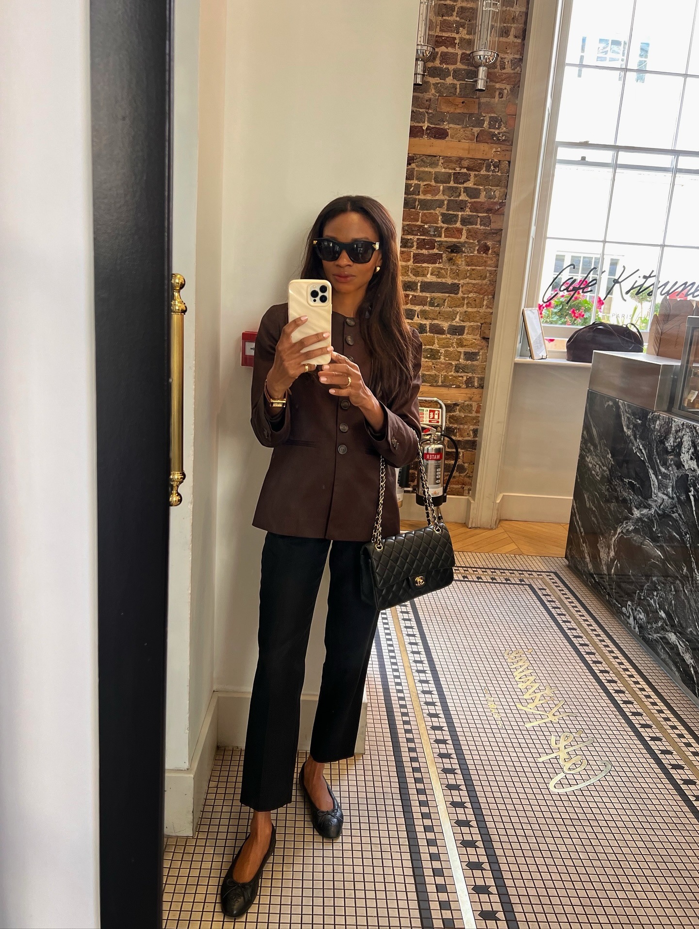 Woman wears black cigarette pants, brown blouse, black Chanel flats and purse.