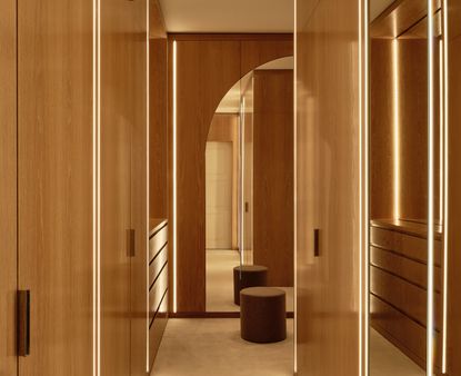 A bedroom with a wooden built in walk in wardrobe with LED strip lights