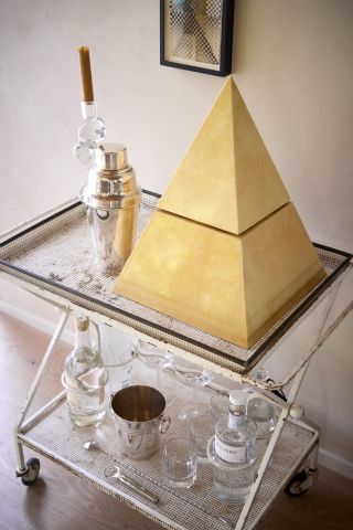 A bar cart with a pyramid shaped wine cooler and a chrome cocktail shaker