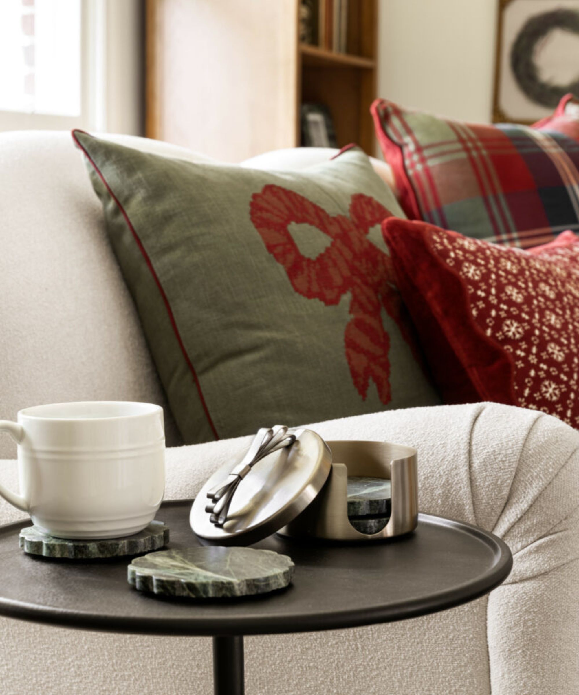 Boucle sofa with green bow cushion and plaid red cushion and side table with mug and marble coasters