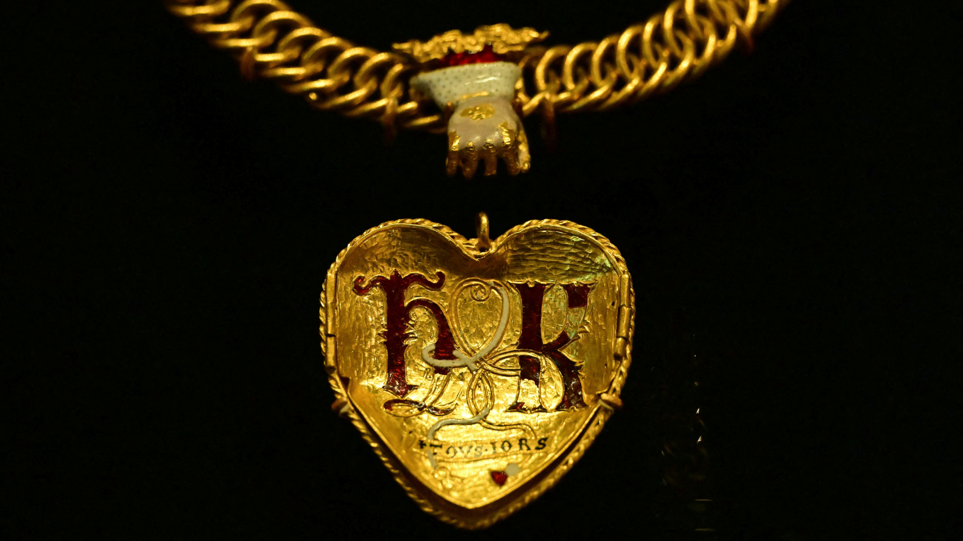 a gold heart-shaped pendant with the letters H and K in red enamel
