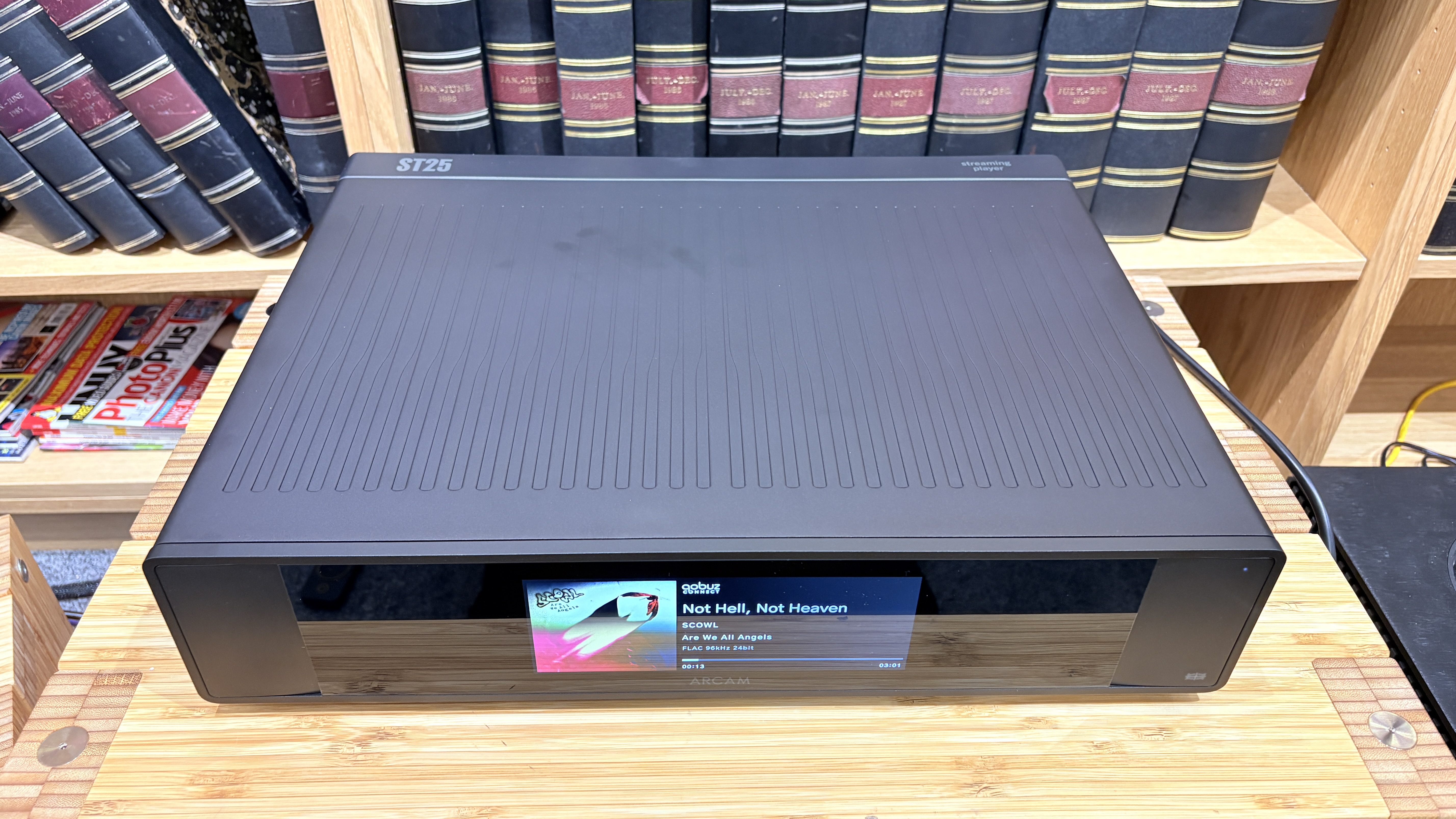 Arcam ST25 music streamer on wooden rack with bookshelf behind it