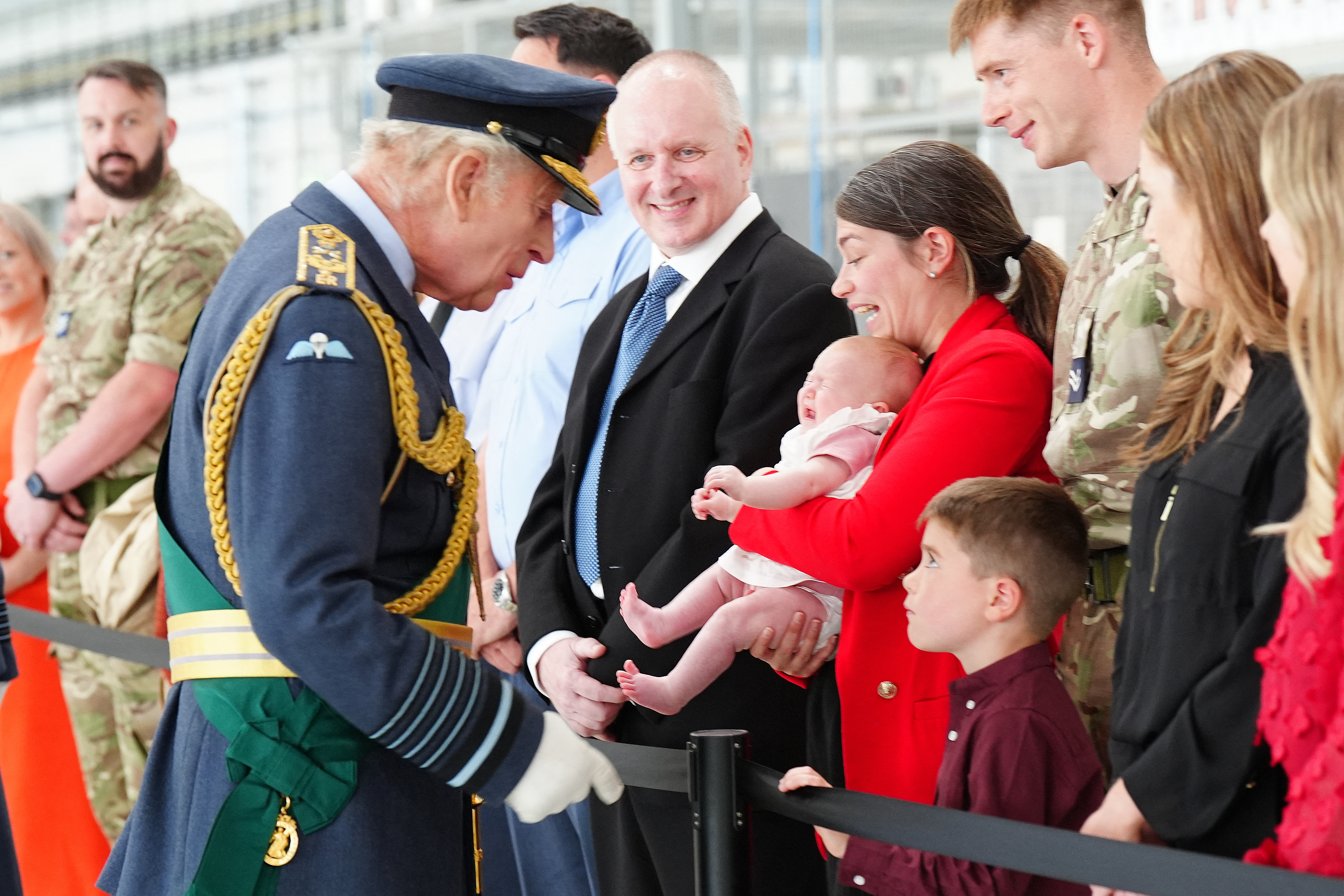 King Charles wears military uniform and meets a crowd of people including an unhappy baby