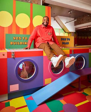 A portrait of Yinka Ilori sitting on one of the washing machines inside his colourful ‘Launderette of Dreams’ pop up space in East London