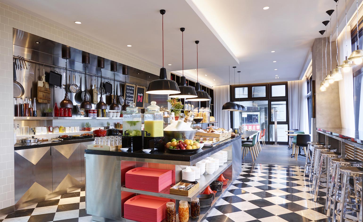CitizenM North Gate kitchen with stainless steel cabinets and island, black marble tops and pans hanging on wall