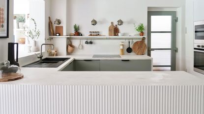 Fluted panel in modern off-white and sage green kitchen with black hardware and microcemented counters