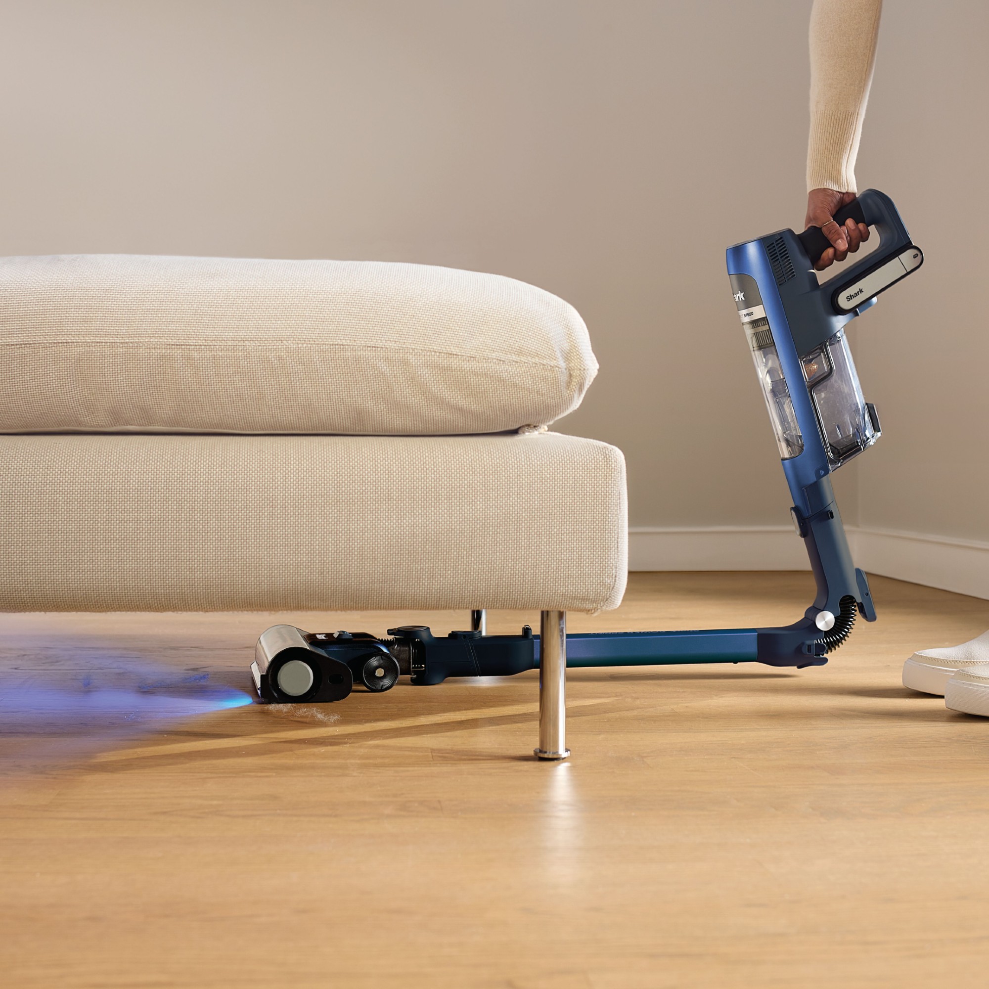 The PowerDetect Speed Clean and Empty Pet Pro cordless vacuum IA3241UKT by Shark being used to vaccum underneath a cream sofa