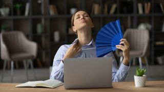 A woman fanning herself in front of a laptop