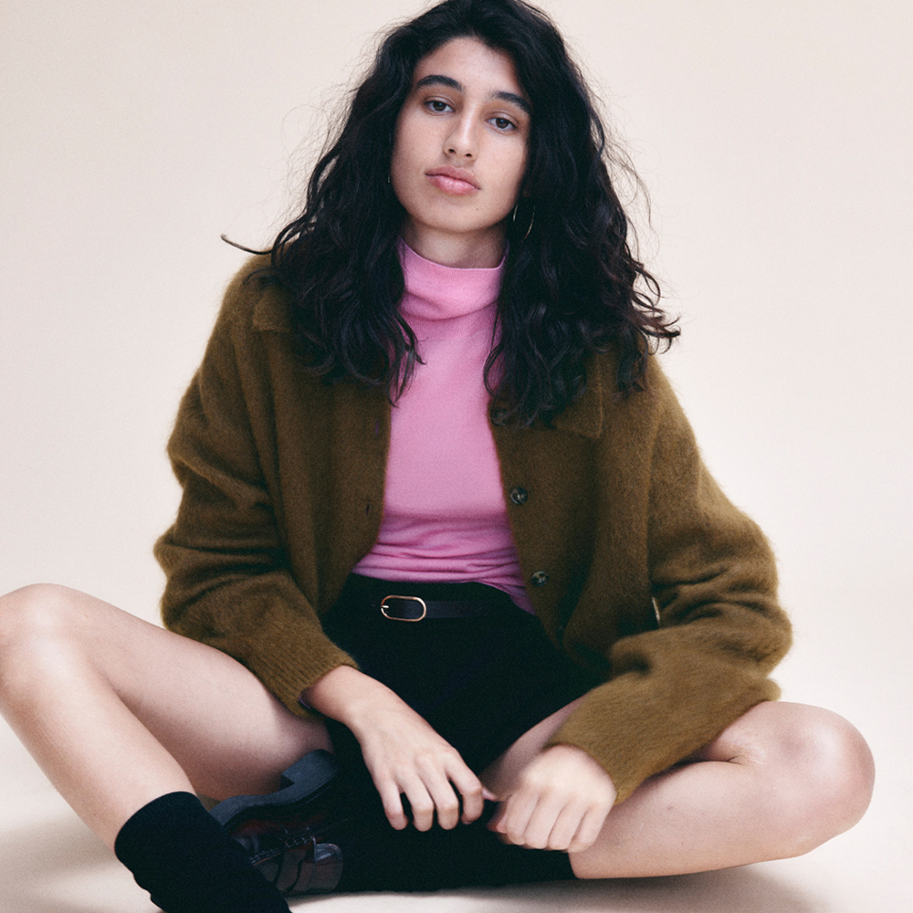Model sat crossed legged wearing a khaki collared cardigan a pink turtle neck and patent leather loafers sold at 
Other Stories
