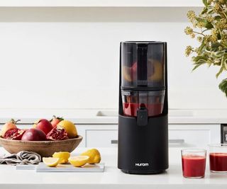 A black Huron juicer on a countertop with fruit to the left of it