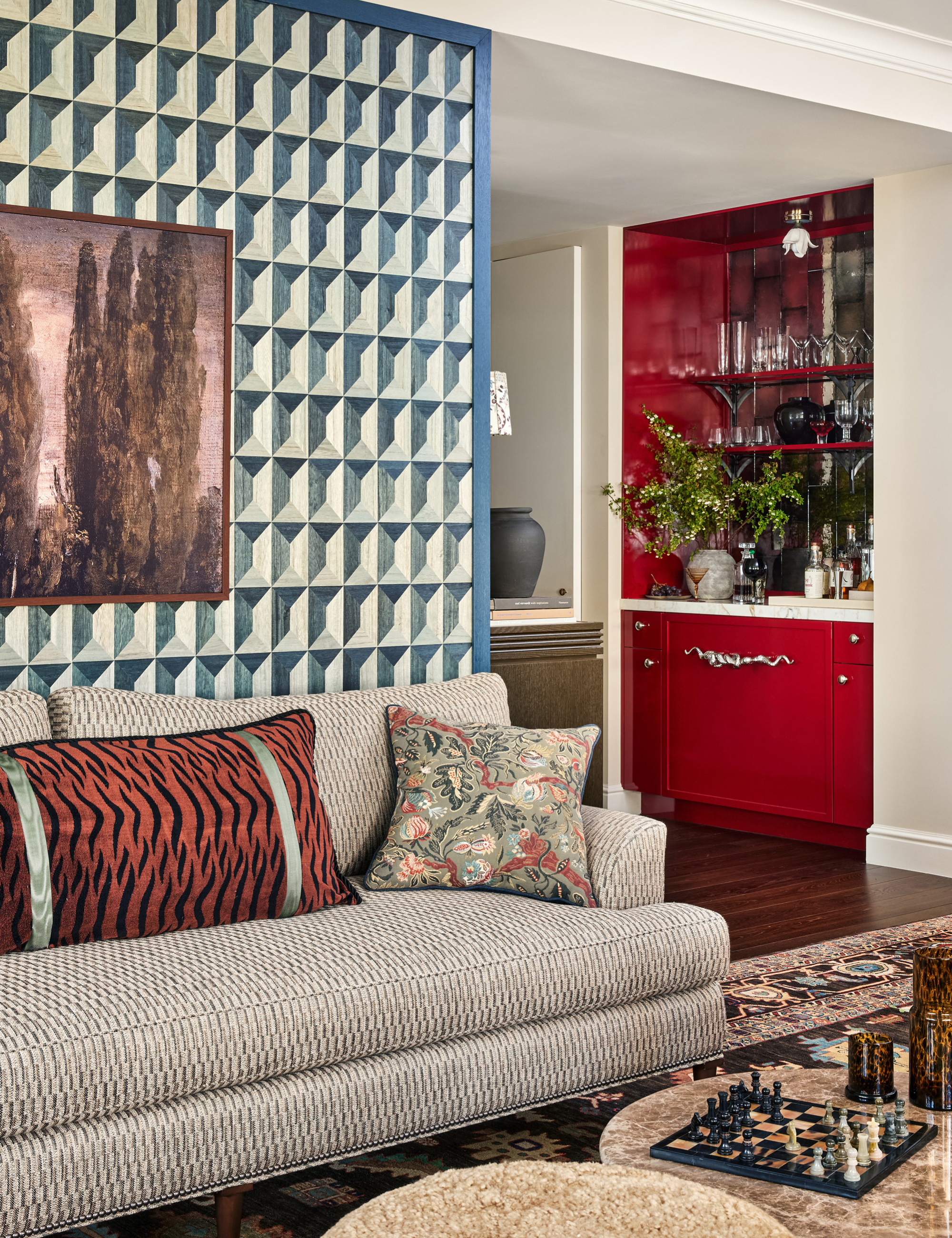Pattern-packed living room area featuring geometric wallpaper, tiger-print pillows, marble coffee tables, and a red bar cabinet