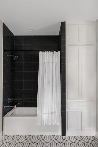 black, white and grey bathroom with black tiles in shower, shower over tub, white shower curtain, patterned floor tiles