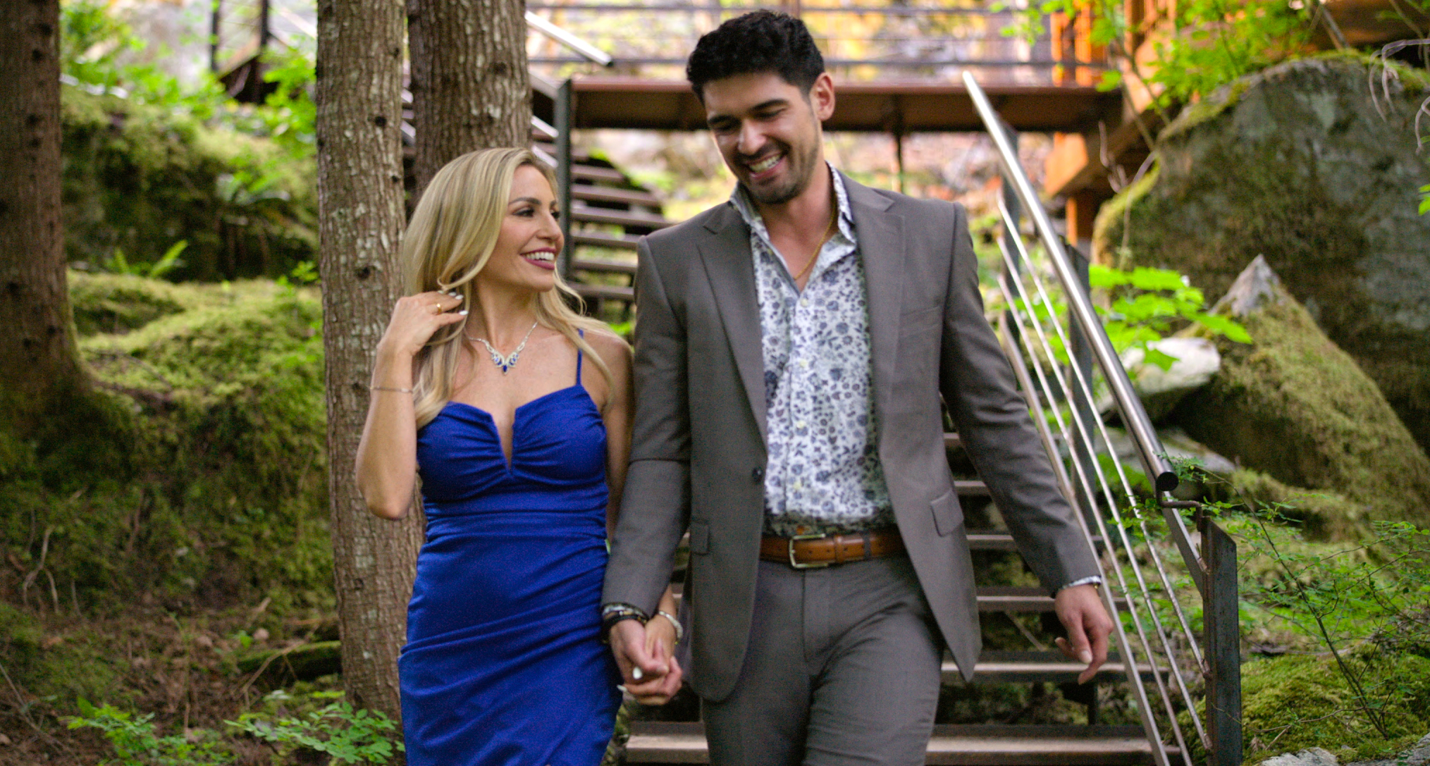 age of attraction stars vanessa and logan walk down a trail in the woods together smiling in a still from the reality show
