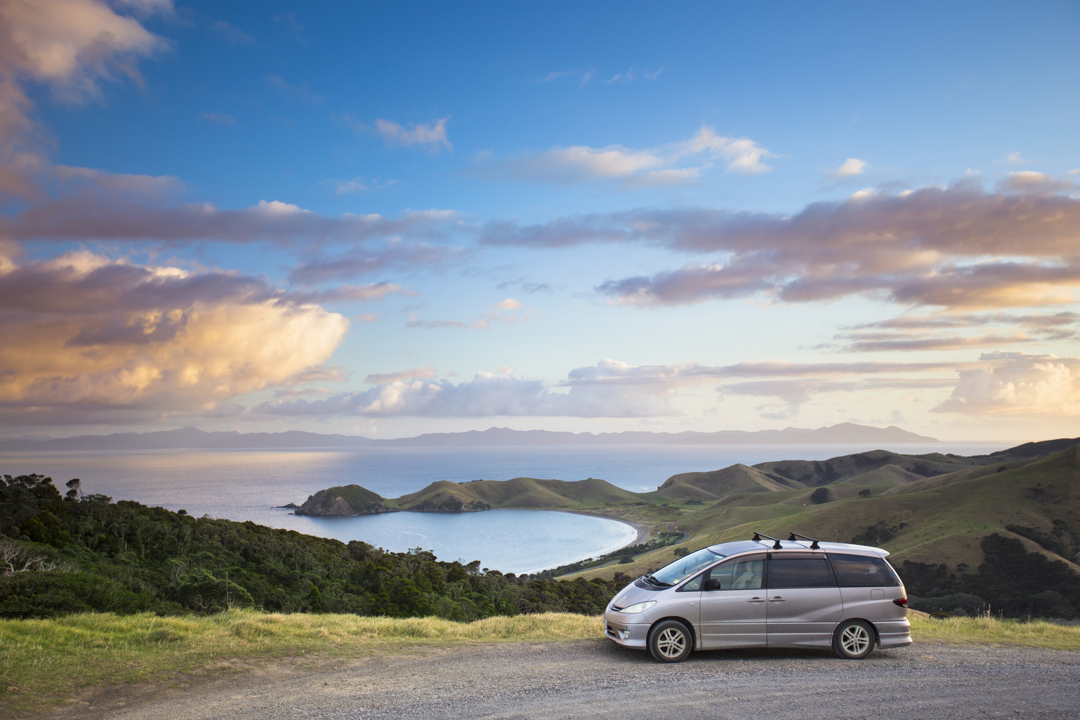 a minivan parked near a park extending to the bayside of an ocean
