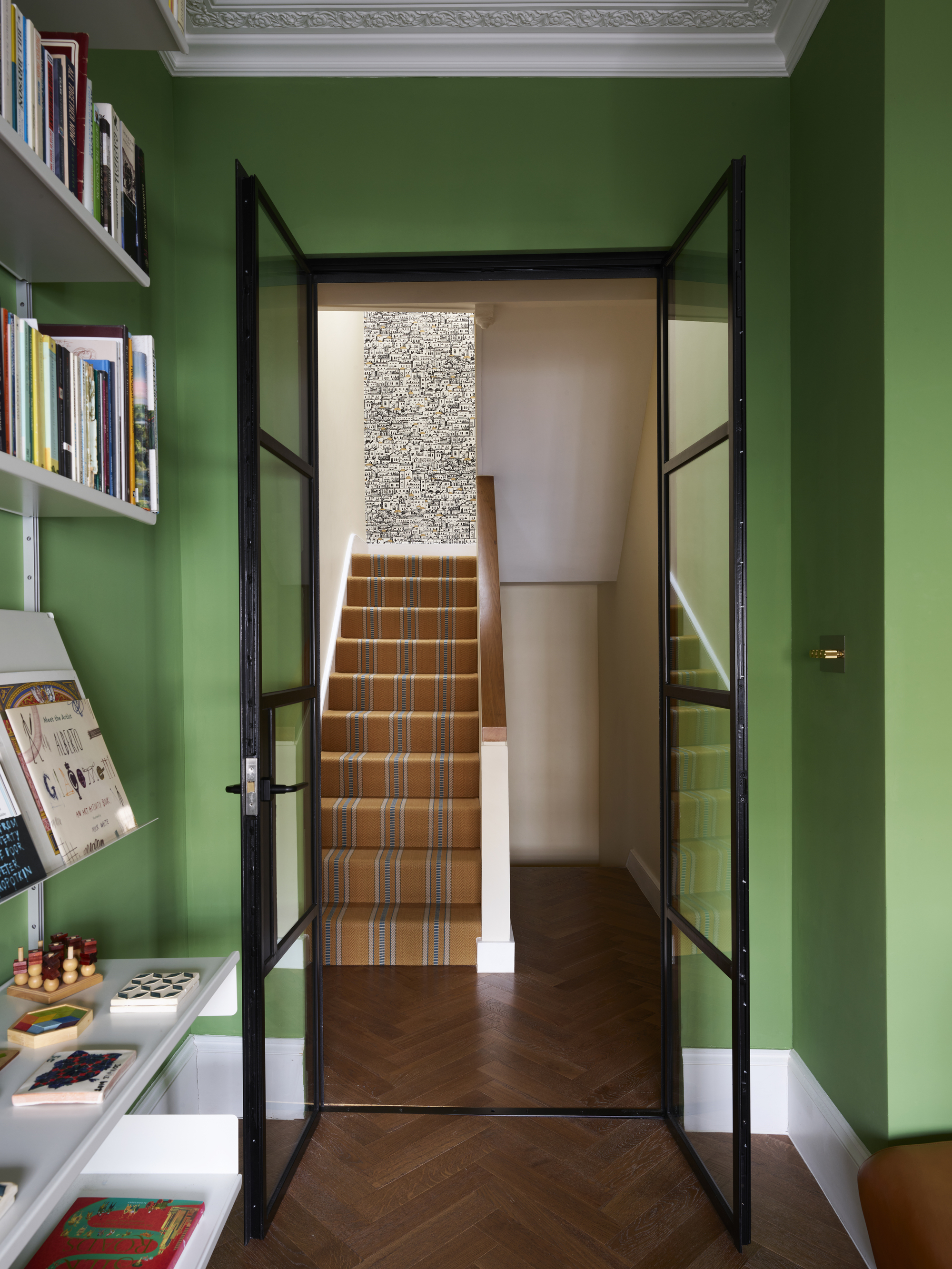 hallway with parquetry floors, green walls, white trim, bookshelf, and stairs with an orange striped runner leading upstairs