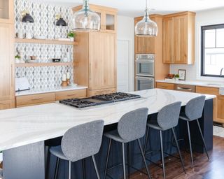 Long kitchen island with smart bar stools, glass pendants, and tiled, patterned feature wall.