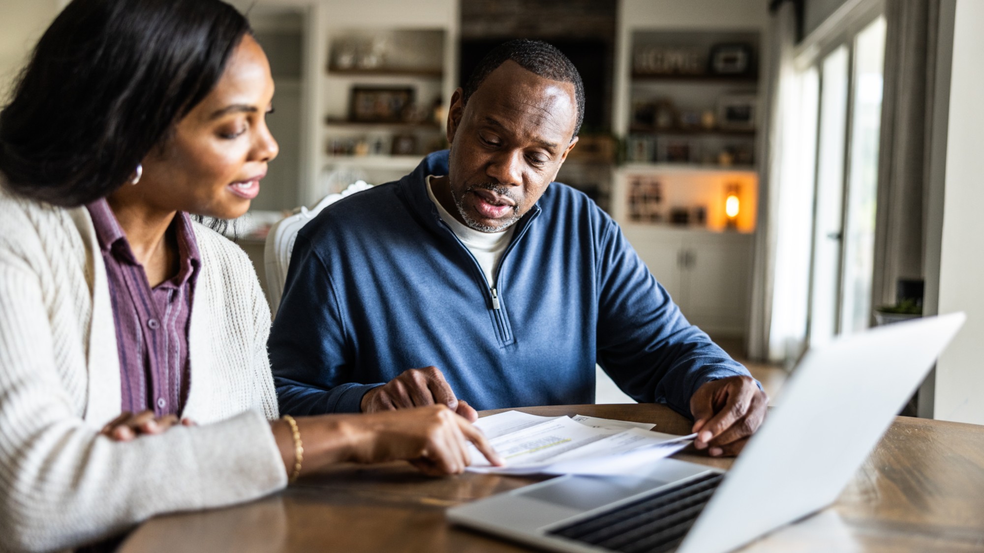Husband and wife looking over bills and using laptop in domestic kitchen