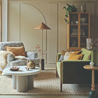 A living room with a panelled wall, a textured rug and various cushions on a green sofa and a floral armchair