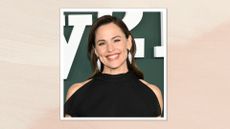 Image of Jennifer Garner smiling with side-part brunette hair behind her back, wearing a cold-shoulder black gown, on a beige pink background