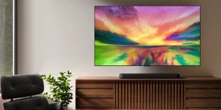 Barre de son LG SE6 posée sur une table en bois sous un téléviseur affichant une image abstraite colorée