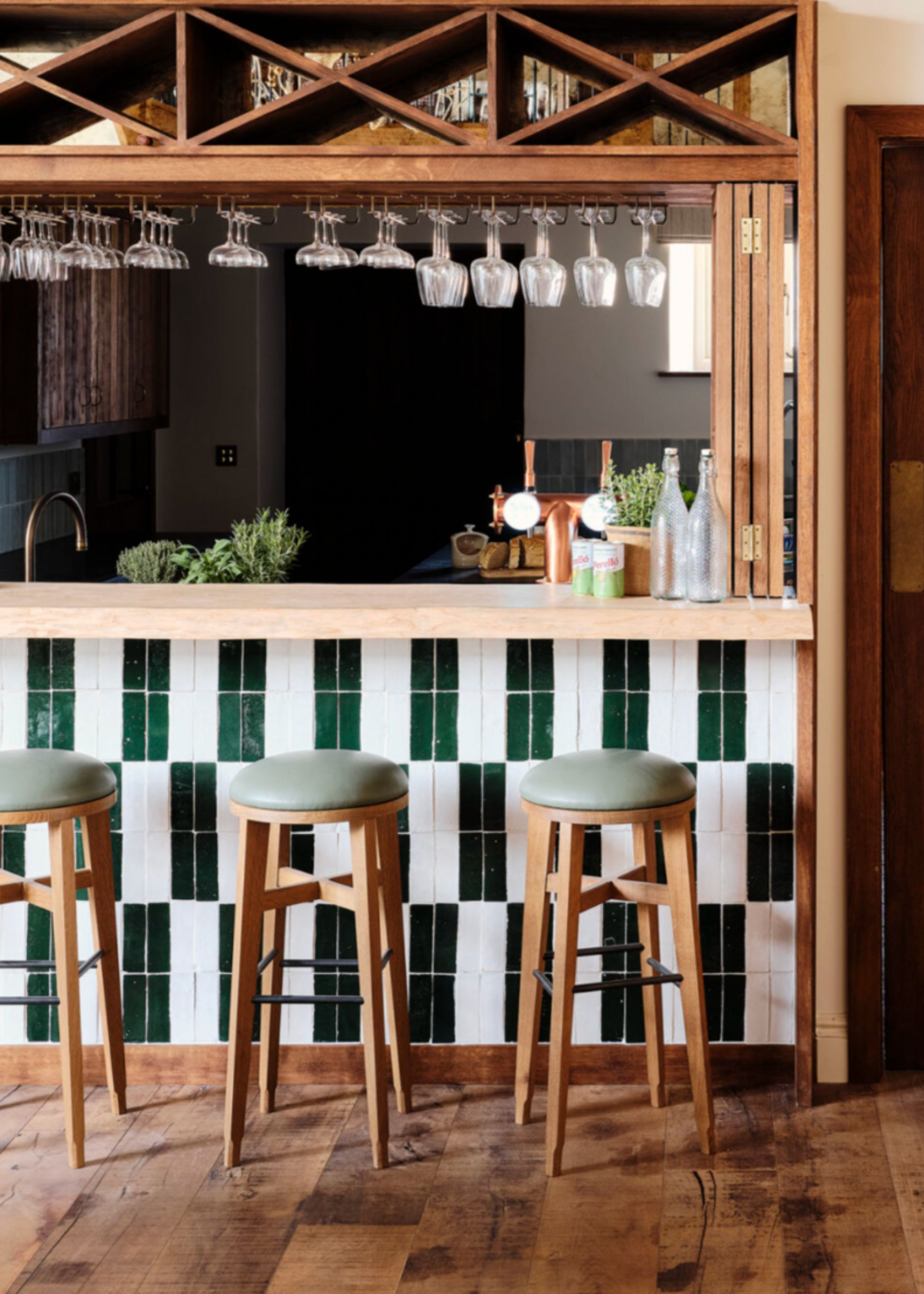A tiled kitchen with three bar stools and a hatch