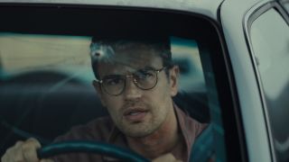 Theo James driving a car with a bullet in the windshield in The Monkey