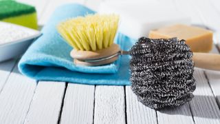 A ball of steel wool next to a scrubbing brush and a microfiber cloth
