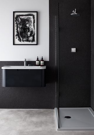 Black bathroom with black shower cubicle, black basin and tiled flooring with monochrome wall art