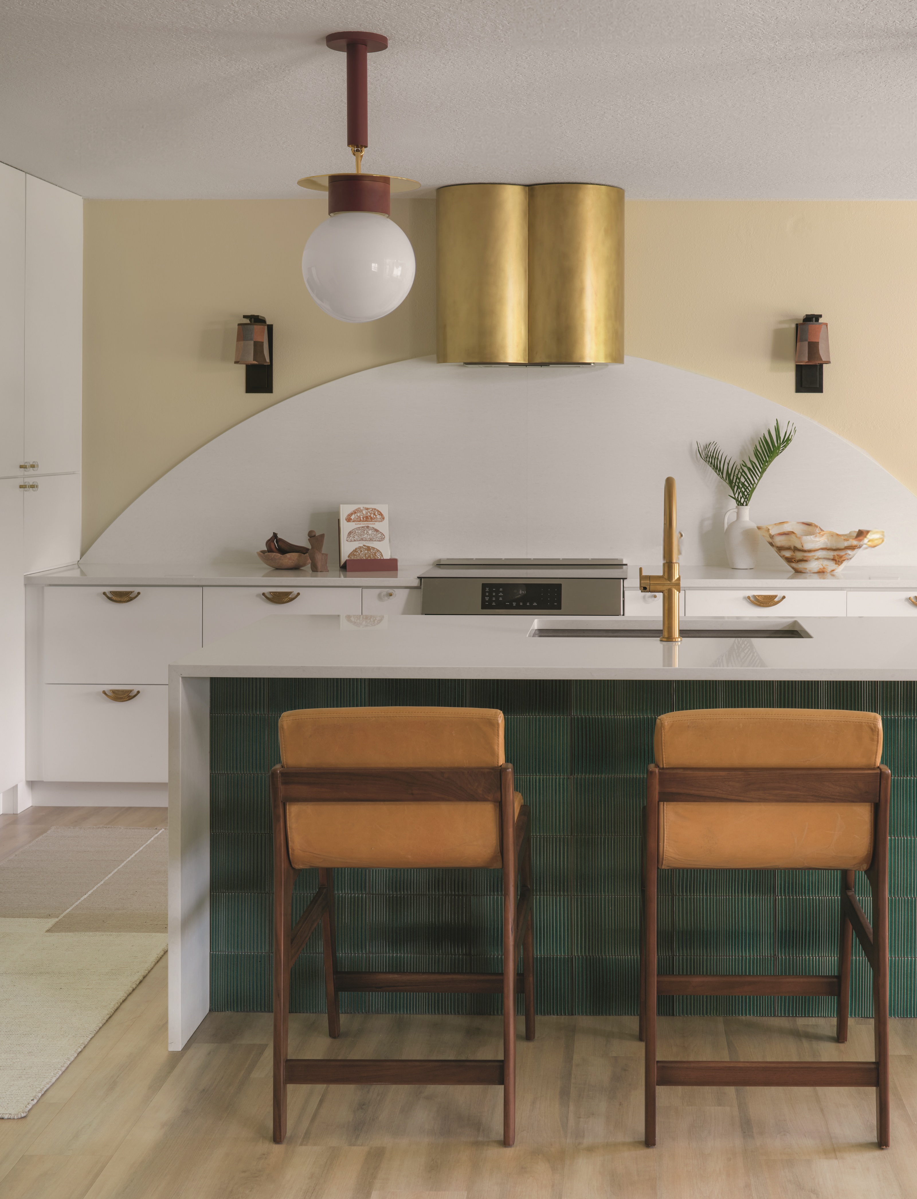 a white kitchen with a curved white backsplash and green emerald tiles on the island