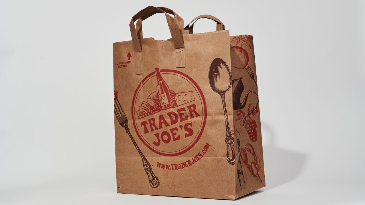 Brown paper bag with handles with Trader Joe&#039;s logo printed on it, on gray studio background