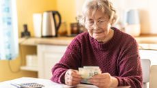 A senior woman counting money in her kitchen