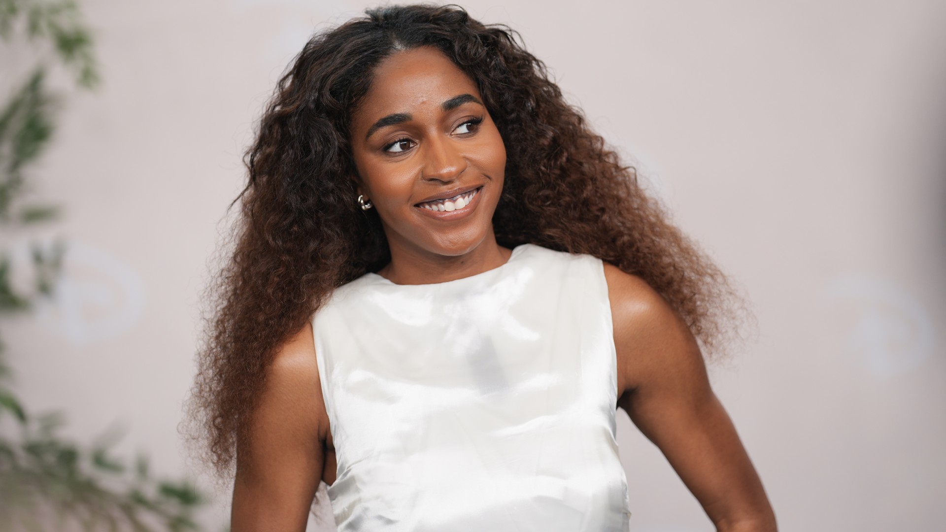 a black woman with long, curly hair wearing a white gown and posing in front of a light background