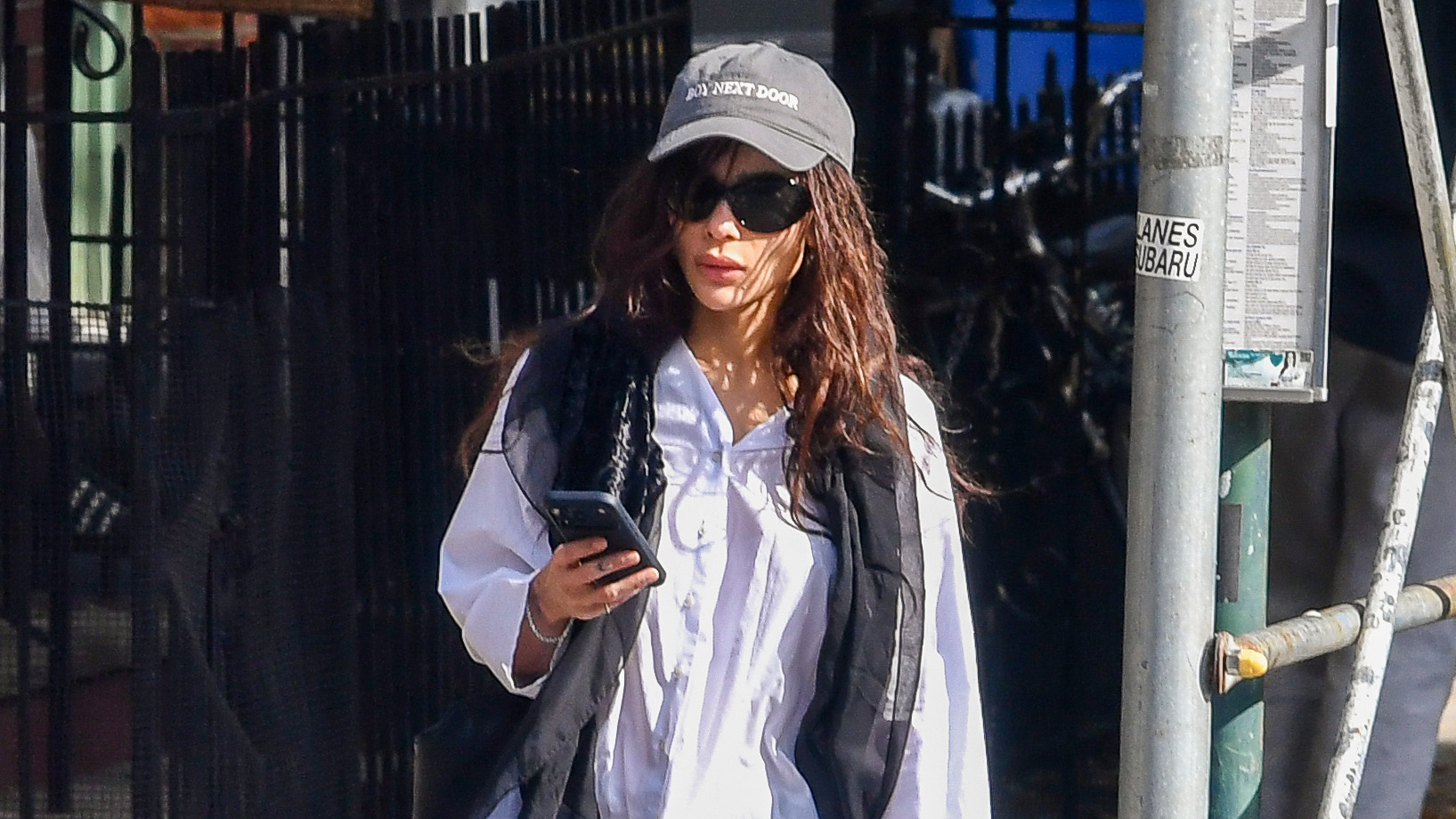Zo&euml; Kravitz wearing a sheer skinny scarf, white button-down shirt, black pants, and black Adidas Samba sneakers